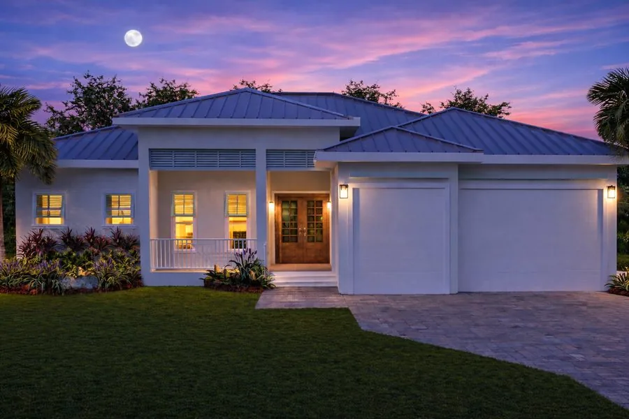 Cloud Design Build custom home at dusk with a standing-seam metal roof and three-car garage in Southwest Florida