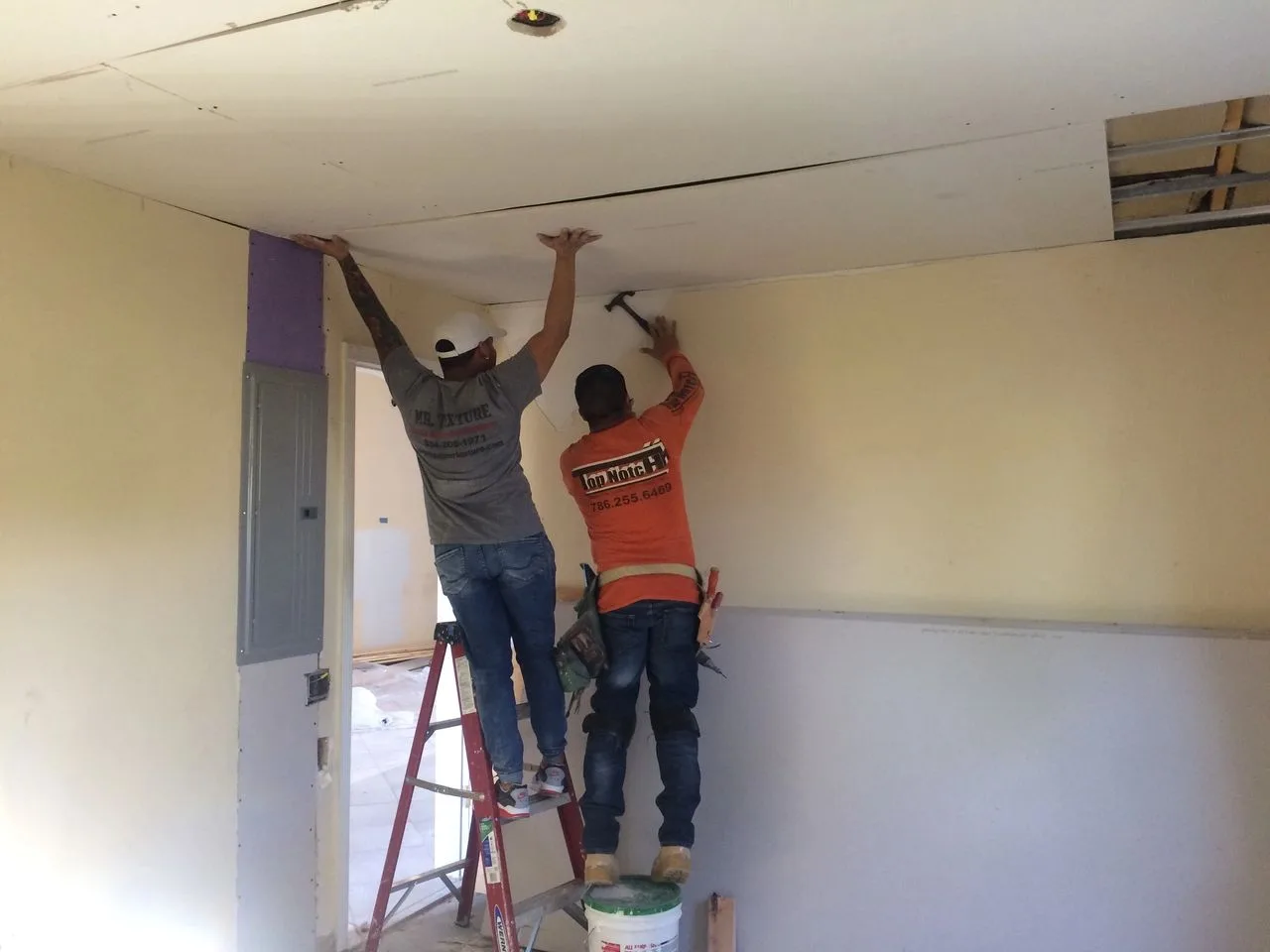 Two contractors patching drywall on a ceiling during interior repair work