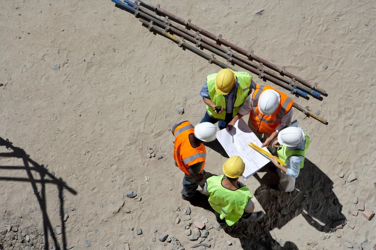 Overhead view of five workers gathered around blueprints at a job site