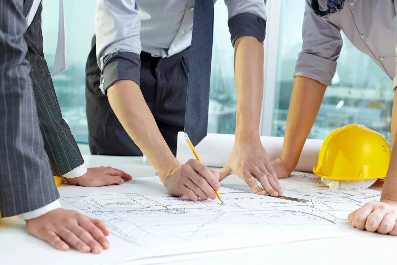 Three professionals reviewing a floor plan blueprint with a hard hat on the table